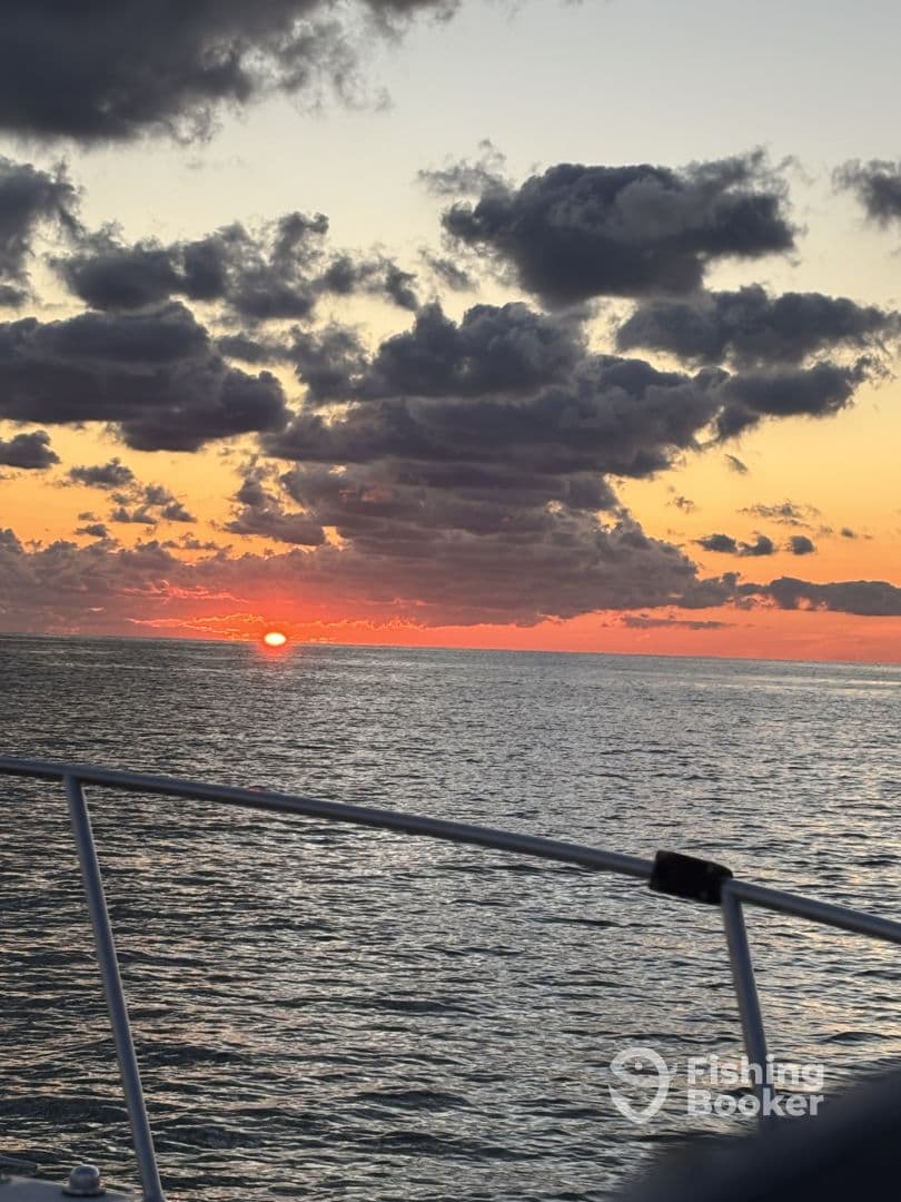 A stunning sunset over the ocean, viewed from a boat, showcasing vibrant colors and dramatic cloud formations.