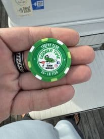 A hand holding a green trophy club chip from Goober Time Guide Service, indicating a catch of 30+ lb fish.