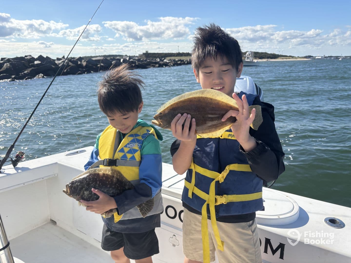 Two young anglers proudly displaying their flounder catch while fishing on a boat, enjoying a sunny day on the water.