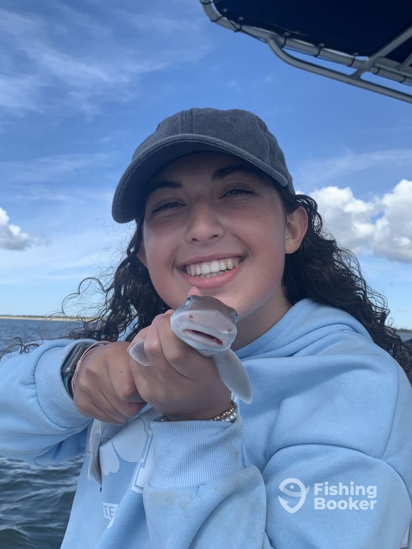 A young angler joyfully displaying a small shark while fishing on a boat, showcasing a fun day on the water.
