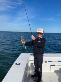 A young angler is reeling in a small fish while fishing on a boat in clear blue waters, showcasing the excitement of the catch.
