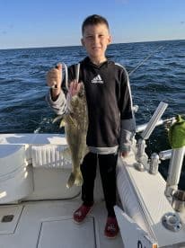 A young angler proudly displaying a Walleye while fishing on a boat, showcasing a successful day on the water.