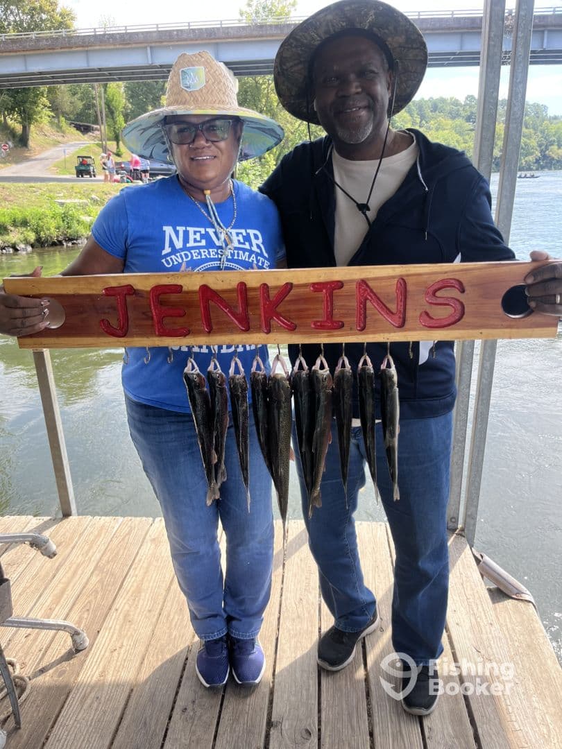 Two anglers proudly displaying their catch of fish on a wooden board at the dock, showcasing a successful fishing trip.