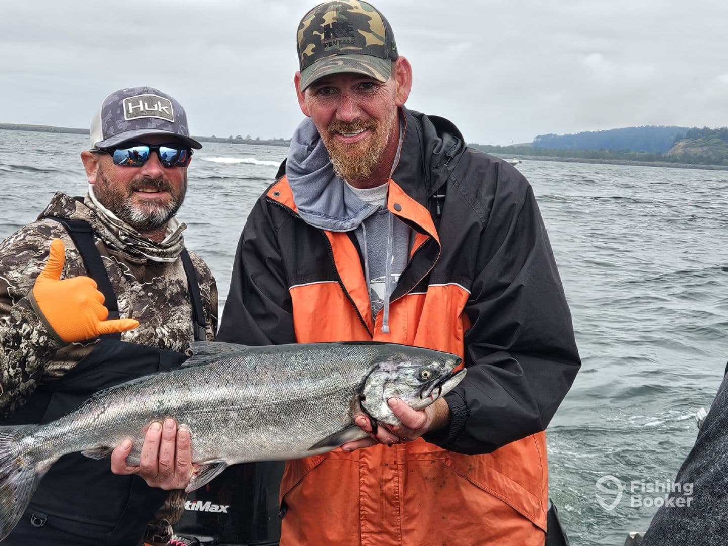 Two anglers proudly displaying a large Salmon while fishing in a coastal environment.