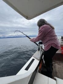 An angler actively reeling in a catch while fishing from a boat in calm waters, showcasing the excitement of the fishing experience.