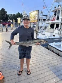Young angler proudly holding a large fish at the dock, showcasing a successful fishing trip.