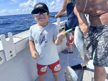 A young angler joyfully holding a fish while fishing on a boat, showcasing a fun family fishing experience.