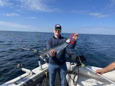 Angler holding a large fish while fishing on a boat in open water, showcasing a successful catch during a day out on the ocean.