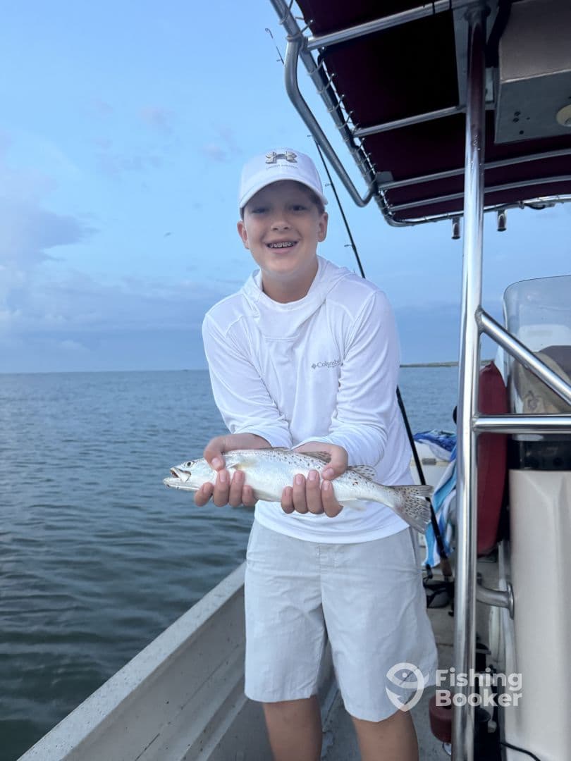 Young angler proudly holding a Speckled Trout while fishing from a boat, showcasing a successful catch during a coastal fishing trip.