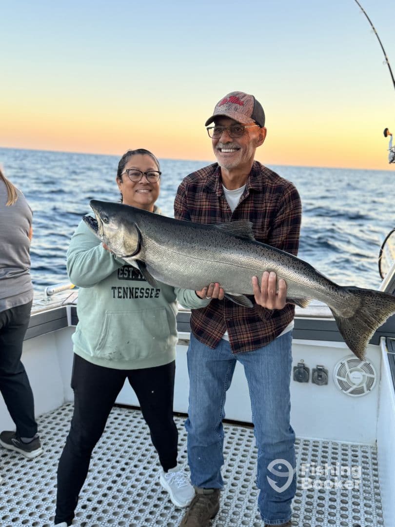 Two anglers proudly displaying a large Salmon on a fishing charter at sunset.
