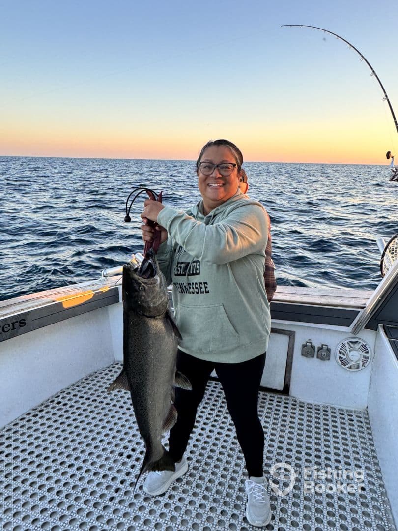 An angler proudly displaying a large Salmon while fishing on a boat during sunset.