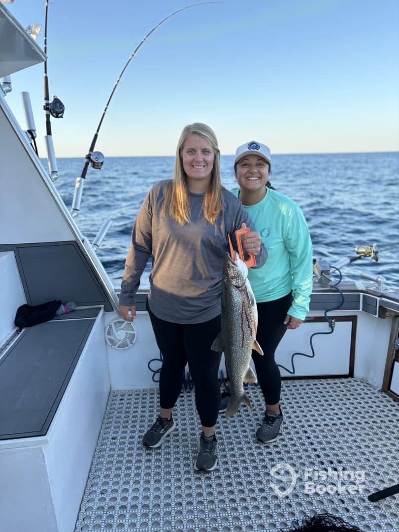 Two anglers proudly displaying a large fish on a fishing boat, showcasing their successful catch during a deep-sea fishing trip.