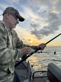 An angler reeling in a catch during a sunset fishing trip on a boat, showcasing the serene atmosphere of the open water.