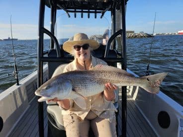 An angler proudly displaying a large Redfish while seated on a boat, enjoying a sunny day on the water.