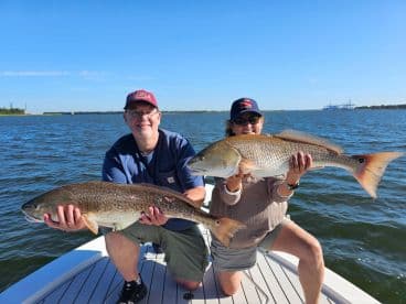 Two anglers proudly displaying their catches of Redfish while enjoying a sunny day on the water.