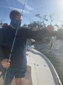 An angler proudly displaying a freshly caught fish while fishing from a boat in a scenic coastal environment.