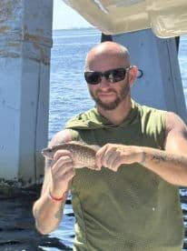 An angler proudly displaying a freshly caught Snapper while fishing near a coastal area.