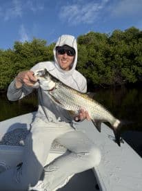 Angler proudly displaying a large Tarpon while fishing in a mangrove area, showcasing the excitement of a successful catch.