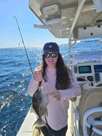 A smiling angler holding a Gray Triggerfish while fishing on a sunny day, showcasing the excitement of a successful catch.