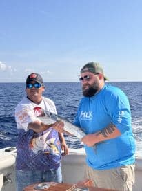 Two anglers proudly displaying a Barracuda while fishing offshore, showcasing a successful day on the water.