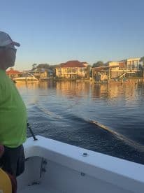 A man enjoying the scenic view from the side of a boat, with waterfront homes in the background during a calm evening.
