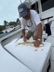A fisherman skillfully filleting a Mahi Mahi on a boat's cleaning station, showcasing the catch after a successful fishing trip.