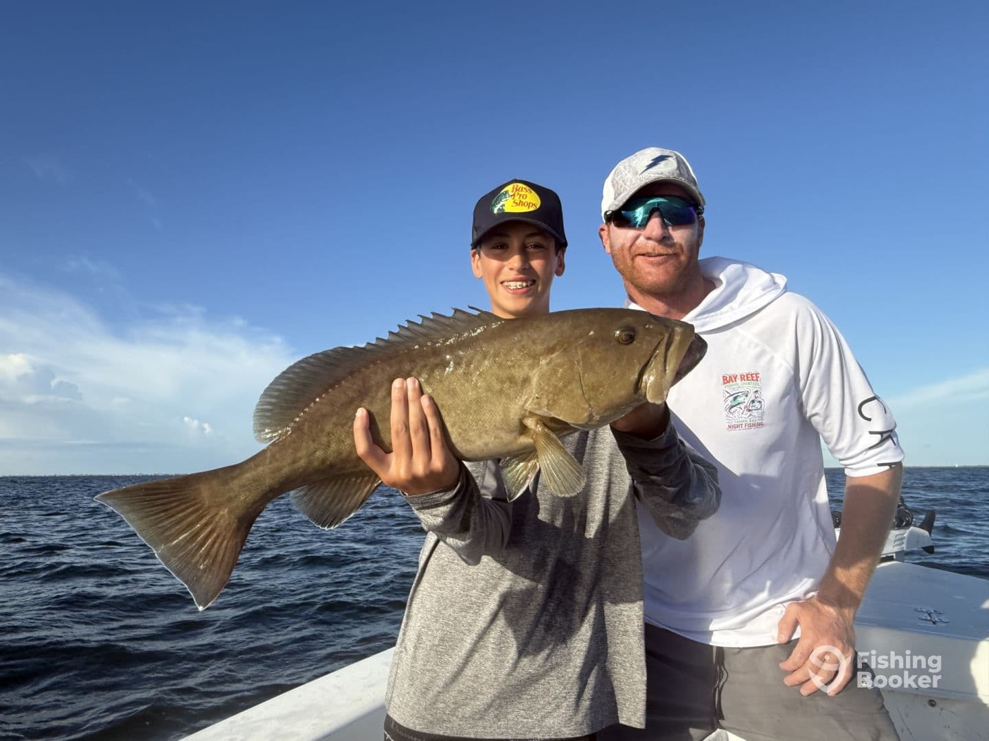 A young angler proudly displaying a large Grouper while fishing on a boat, showcasing a successful day on the water.