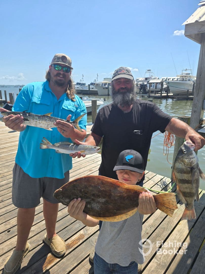 A family proudly displaying their catch of the day, including a large Flounder and other fish, at the dock after a successful fishing trip.