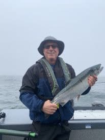 An angler proudly displaying a Silver Salmon while fishing in foggy conditions on a charter boat.