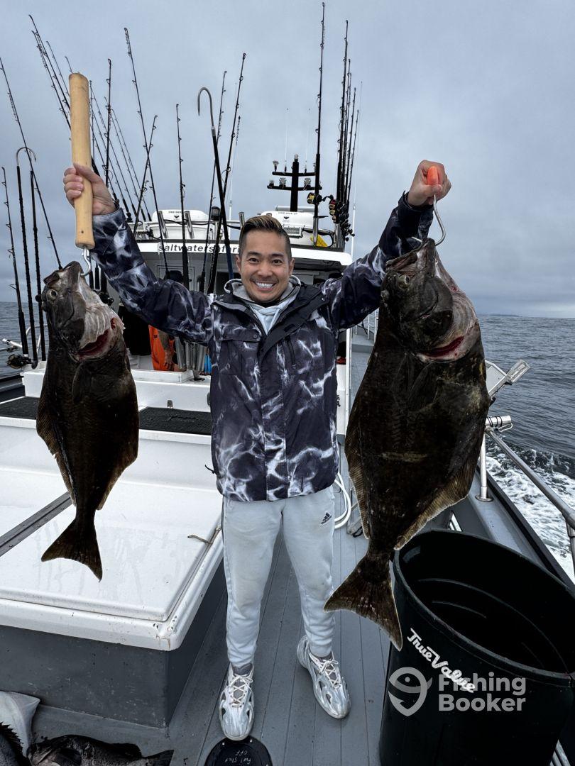Angler proudly displaying two large Halibut on a fishing charter, showcasing a successful day on the water.