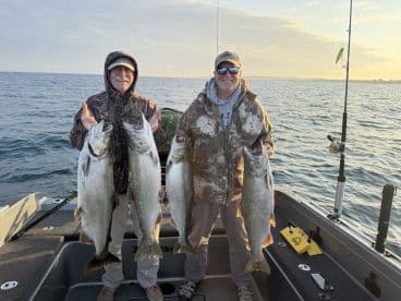 Two anglers proudly displaying their catch of large Lake Trout while fishing on a boat during a serene morning on the water.