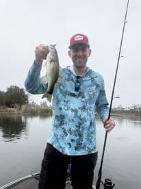 An angler proudly displaying a Largemouth Bass while fishing on a calm lake, showcasing a successful catch.