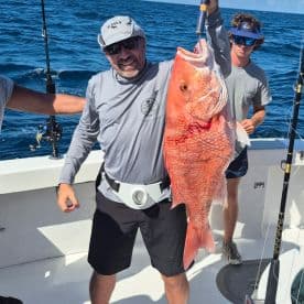 An angler proudly displaying a large Red Snapper while fishing offshore, with another angler in the background.