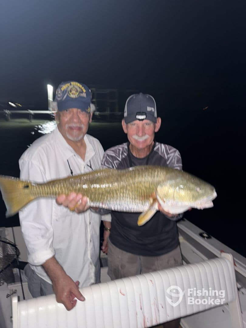 Two anglers proudly displaying a large Redfish aboard their boat during a night fishing trip.
