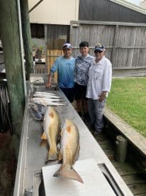 A family poses with their catch of Redfish laid out on a cleaning table at a fishing dock, showcasing a successful day on the water.