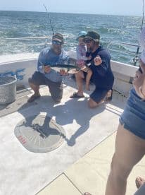 A family enjoys a successful fishing trip, showcasing a caught fish on a boat in open waters.