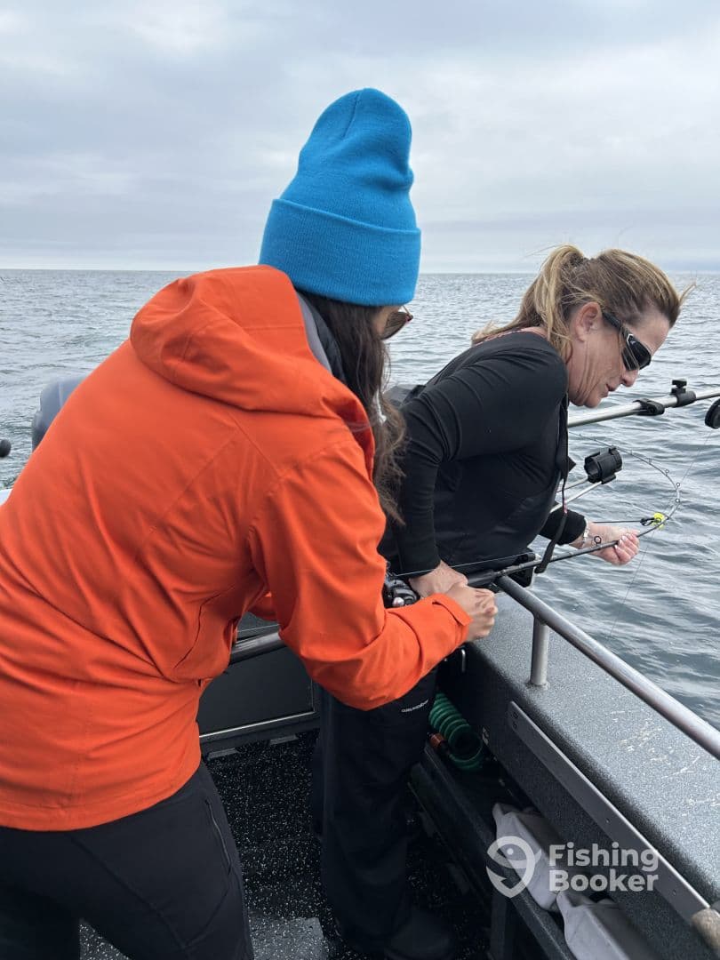 Two anglers engaged in reeling in a catch while fishing on a boat in open water, showcasing a collaborative fishing experience.