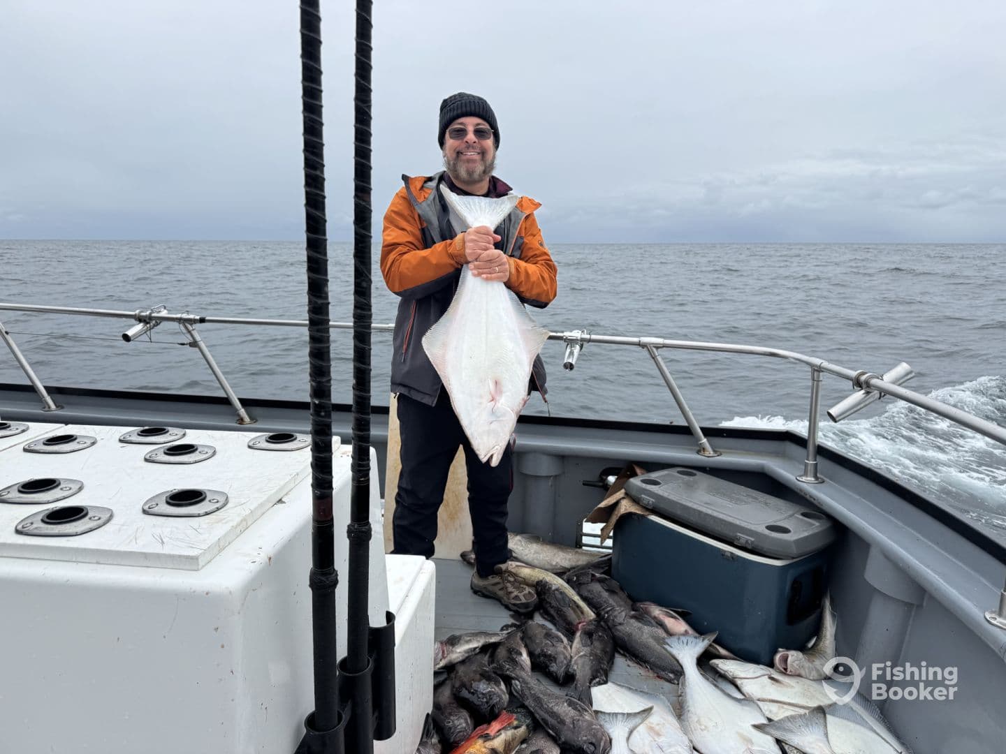 Angler displaying a large Halibut on a fishing boat, surrounded by a variety of other fish after a successful deep-sea fishing trip.