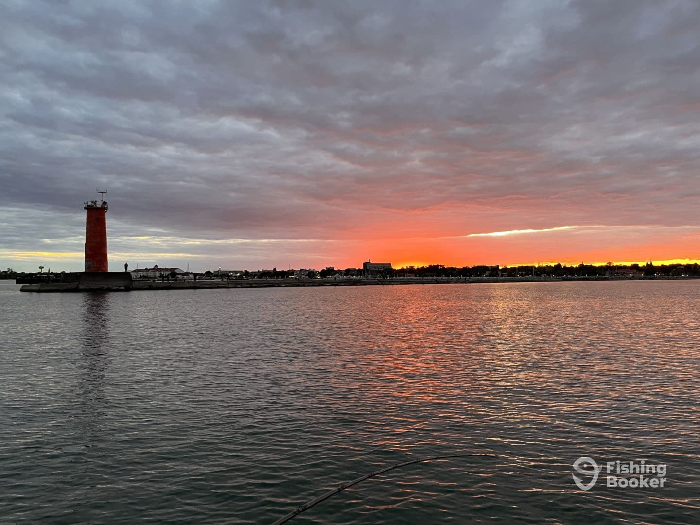 A picturesque sunset over the harbor, featuring a prominent lighthouse and calm waters, ideal for evening fishing trips.
