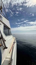 A side view of a fishing boat on calm waters, showcasing a clear sky and distant boat in the background.