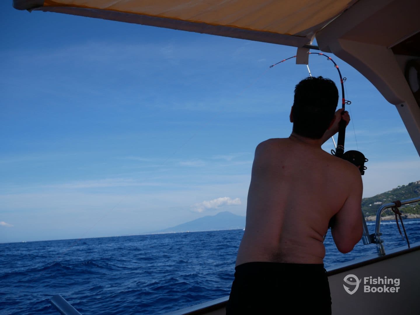 An angler is actively reeling in a fish while fishing on a boat in open water, showcasing the excitement of the catch.
