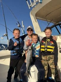 A father and his three sons proudly displaying a large fish while enjoying a day of fishing on the ocean.