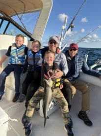 A group of young anglers and adults enjoying a successful fishing trip, with one child proudly displaying a large fish on a boat.