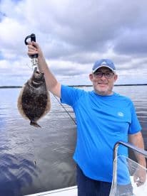 An angler proudly displaying a Flounder caught while fishing on a calm waterway.