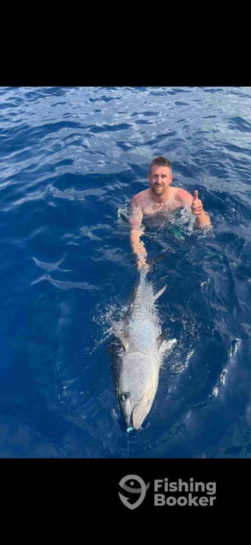 Angler giving a thumbs up while holding a large fish in deep blue waters, showcasing a successful catch during a fishing trip.