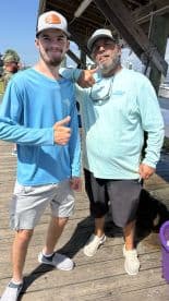 Two individuals posing on a dock, likely after a fishing trip, with no visible catch in the image.