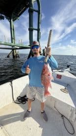 Angler displaying a large Red Snapper while fishing near a structure in open water.