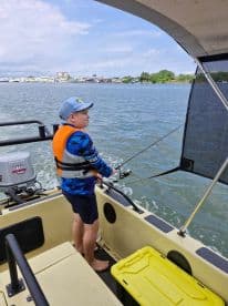 A young angler casting from a small boat, enjoying a fishing adventure in calm waters, wearing a life jacket and fishing gear.