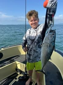 Young angler proudly holding a large fish while fishing from a boat in open waters.