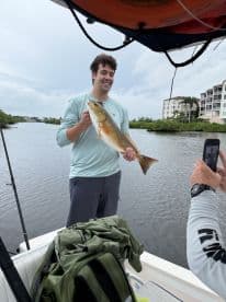 A young man proudly displaying a Redfish while fishing in a scenic coastal waterway, showcasing a successful catch during a charter trip.